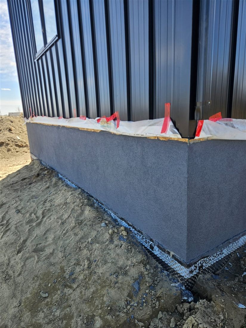 Charcoal parged foundation beside a deck and railing